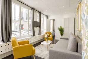 Une chambre d’hôtel moderne avec un canapé, deux fauteuils jaunes, une petite table ronde et une plante en pot.