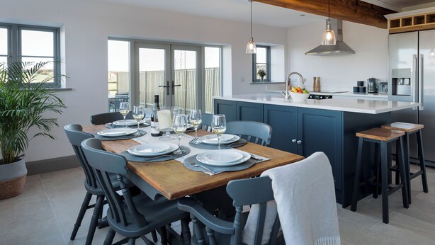 A modern kitchen with a central island, dining table set for six, and a large window. - The Maddocks - UK36311 (Whitchurch)
