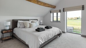 A bedroom with a large bed, two bedside tables, a wooden beam ceiling, a window with a view, and a door leading outside. - The Maddocks - UK36311 (Whitchurch)