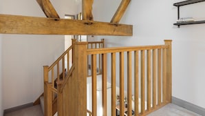 A wooden staircase with a railing, a ceiling light fixture, and a small shelf with books. - The Maddocks - UK36311 (Whitchurch)