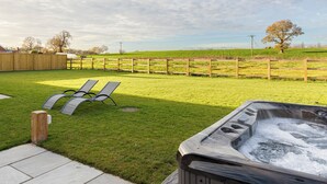 A hot tub in a grassy outdoor area with a wooden fence and a tree in the background. - The Maddocks - UK36311 (Whitchurch)