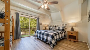 A bedroom with a large bed, a ceiling fan, a nightstand, and a view of the outdoors. - Woodsy cabin perfect for a couple or a group! (Hot Springs)
