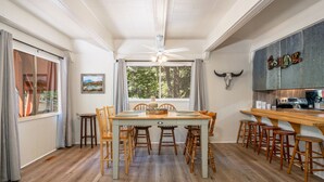 A dining area with a wooden table and chairs, a ceiling fan, and a view of the outdoors through a large window. - Woodsy cabin perfect for a couple or a group! (Hot Springs)