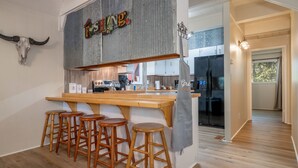 A kitchen with a wooden bar and stools, a refrigerator, and a sign above the bar. - Woodsy cabin perfect for a couple or a group! (Hot Springs)