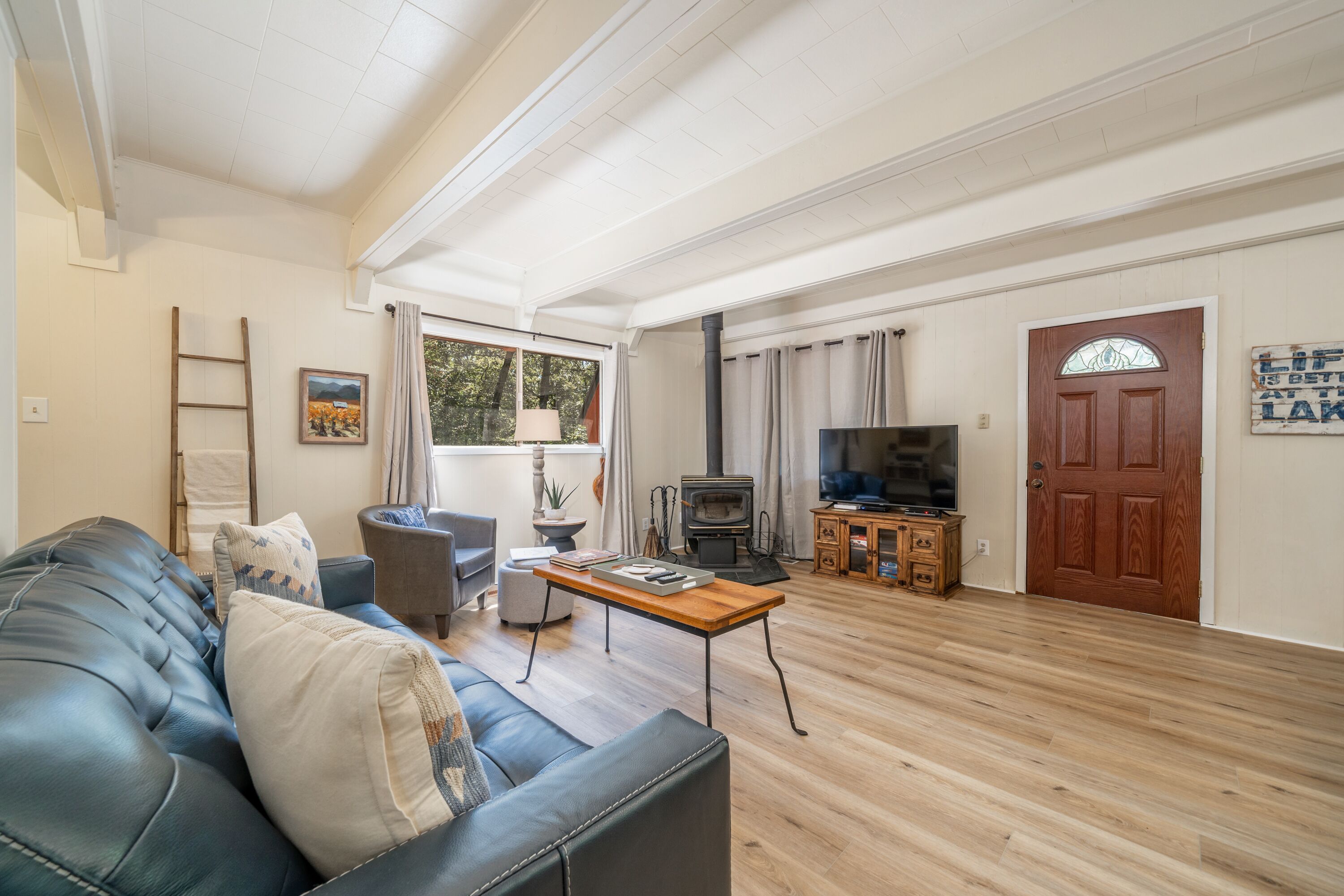 A living room with a leather sofa, wooden coffee table, and a TV. There's a fireplace, a door with a sign, and a window with curtains. - Woodsy cabin perfect for a couple or a group! (Hot Springs)