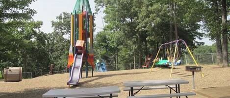A playground with a rocket-shaped slide, picnic tables, and swings.