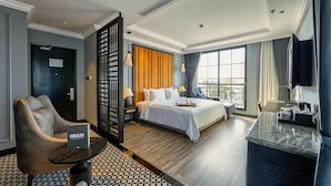 A hotel room with a bed, a desk, a chair, a small table, and a window with curtains. - Hotel DMelin (Ho Chi Minh City)