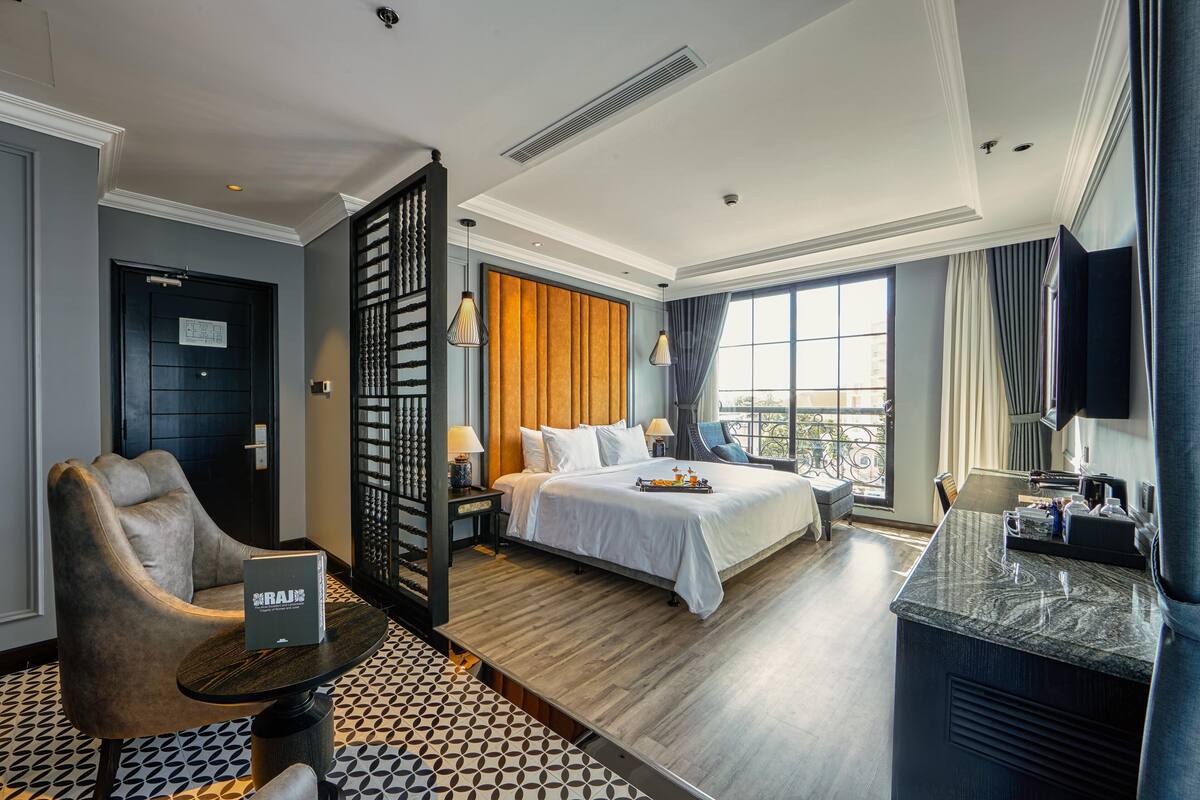 A hotel room with a bed, a desk, a chair, a small table, and a window with curtains.