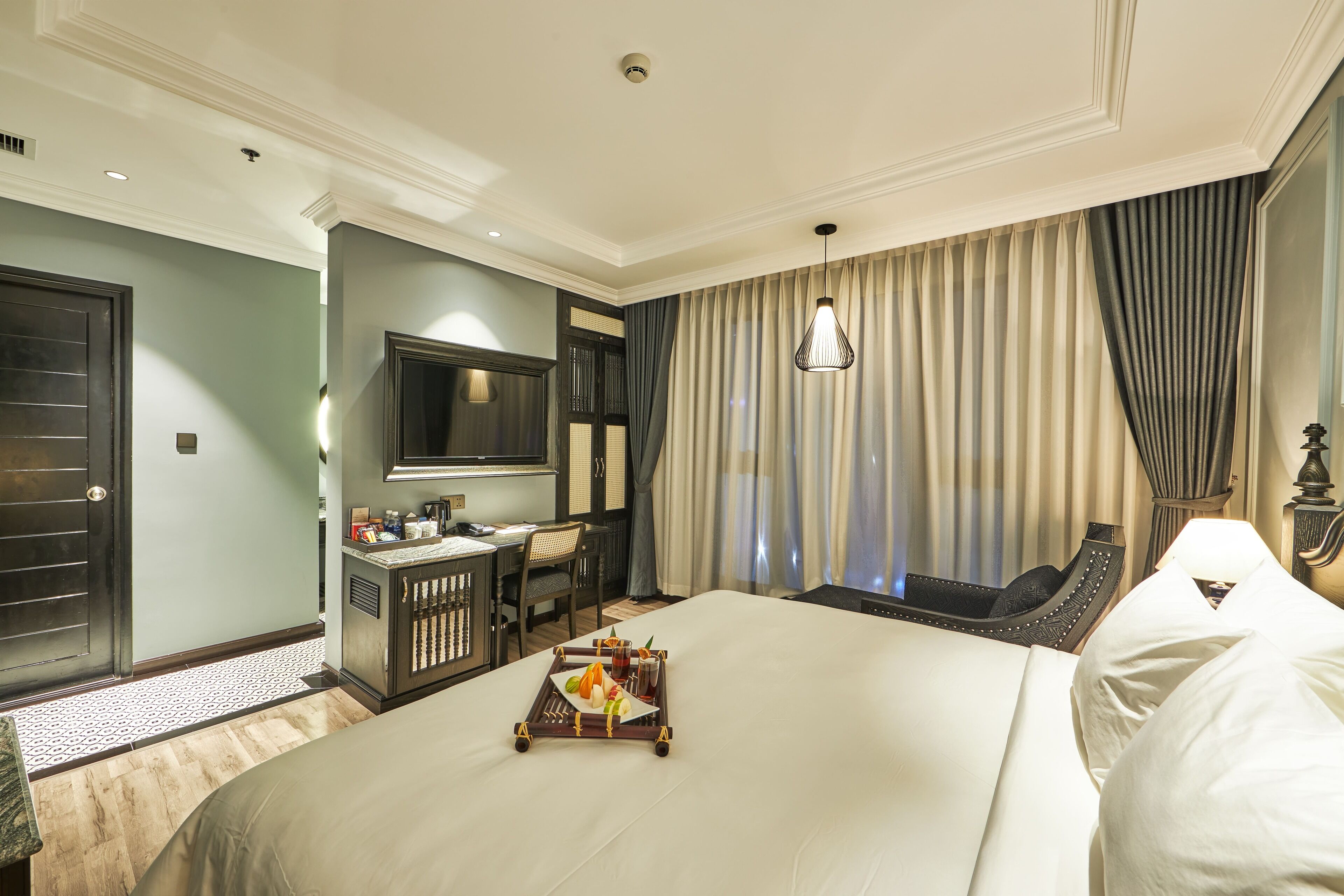 A hotel room with a large bed, a desk with a chair, a television, and a tray with food and drinks.