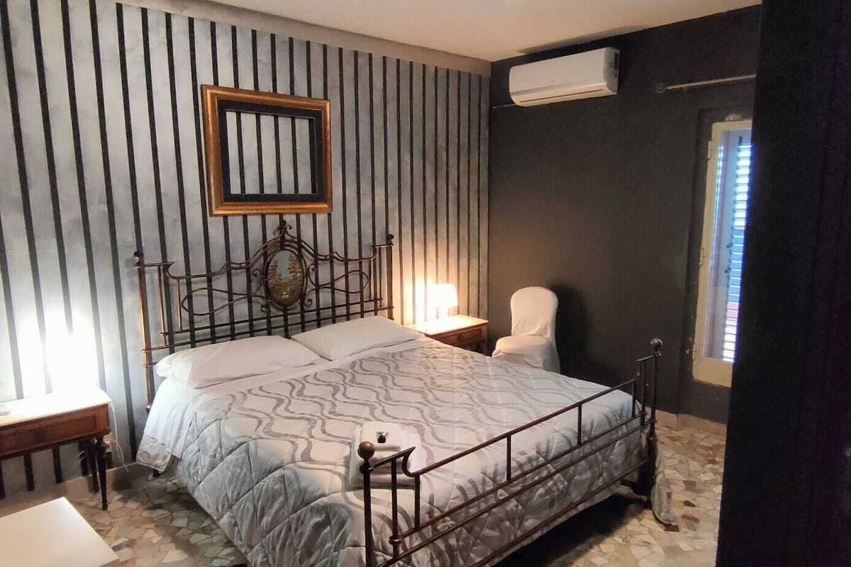 A bedroom with a bed, bedside table, lamp, and a window with blinds.