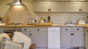 A modern kitchen with white cabinets, a stainless steel range hood, a dishwasher, and a countertop with a toaster and a kettle. - The Old Cobblers Cottage (Bakewell)