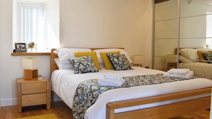 A neatly arranged bedroom with a wooden bed, a bedside table, a nightstand, a mirror, and a window with blinds. - Y Bwthyn at Tyddyn Obry (Ty Croes)