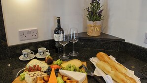 A kitchen counter with a cheese board, wine glasses, a bottle of wine, a loaf of bread, and a potted plant. - Y Bwthyn at Tyddyn Obry (Ty Croes)