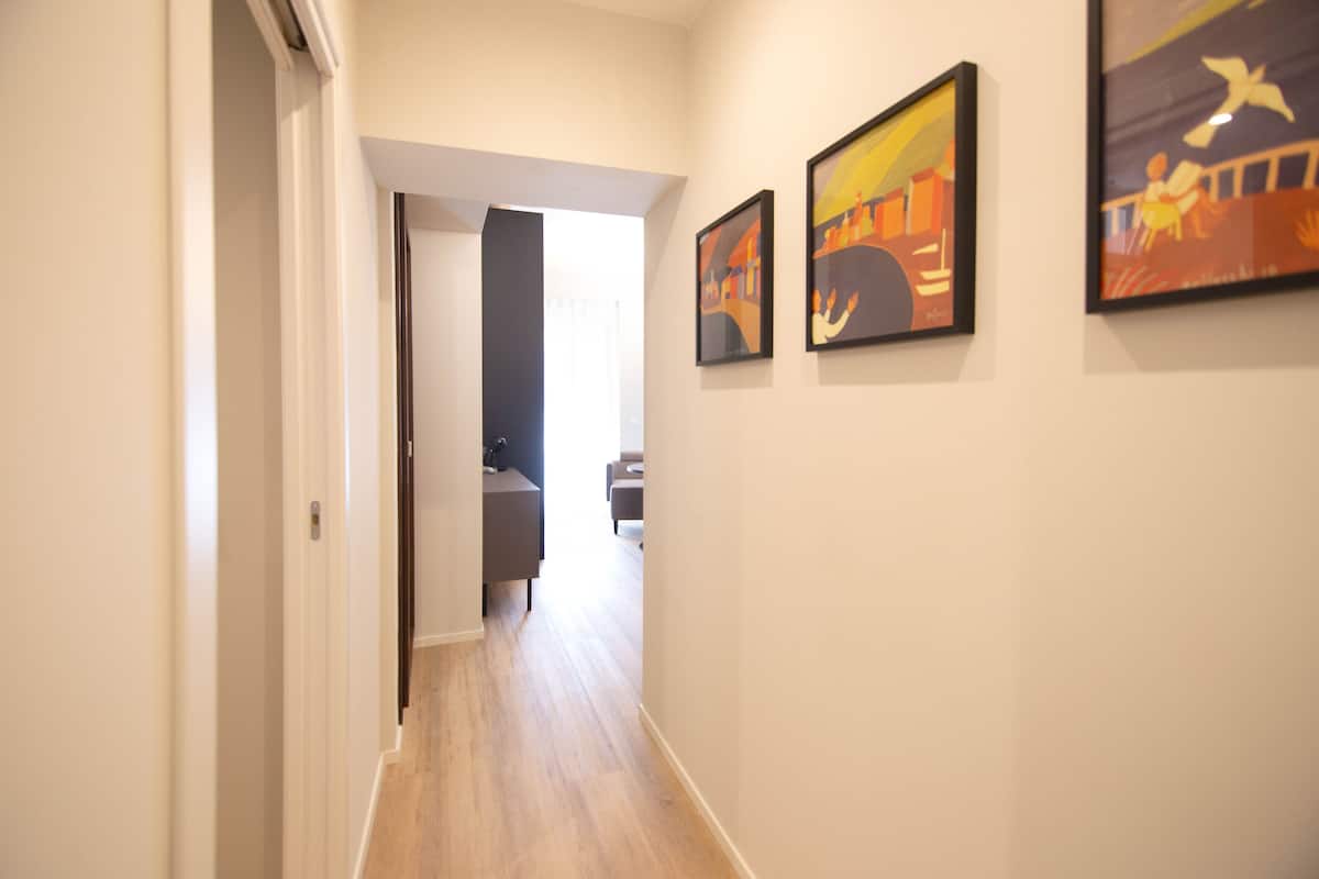 Un couloir avec un plancher en bois, une porte sur le côté gauche et trois œuvres d’art encadrées sur le mur de droite.