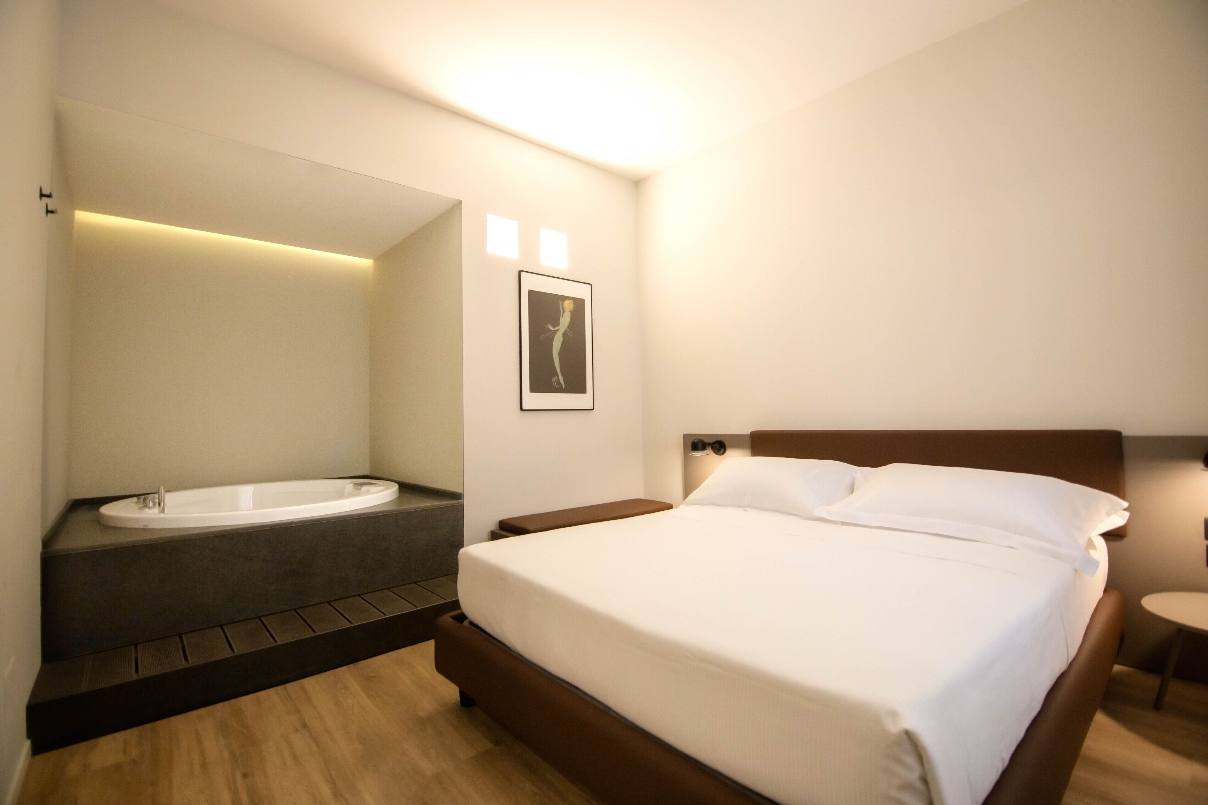 A modern hotel room with a large bed, a built-in bathtub, and a small bedside table.