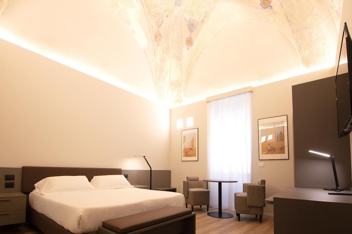 Une chambre d’hôtel moderne, dotée d’un grand lit, de tables de chevet, d’un bureau et d’une chaise.