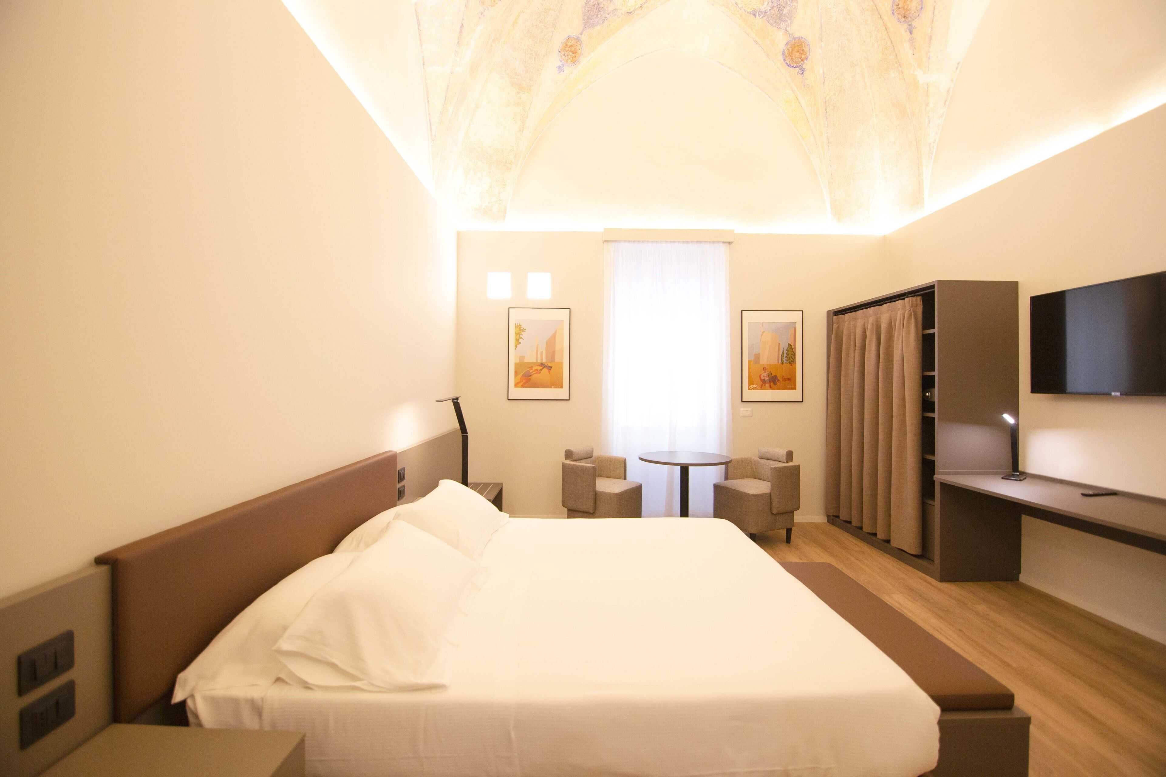 Een hotelkamer met een groot bed, een bureau met stoel, een klein tafeltje en een televisie.