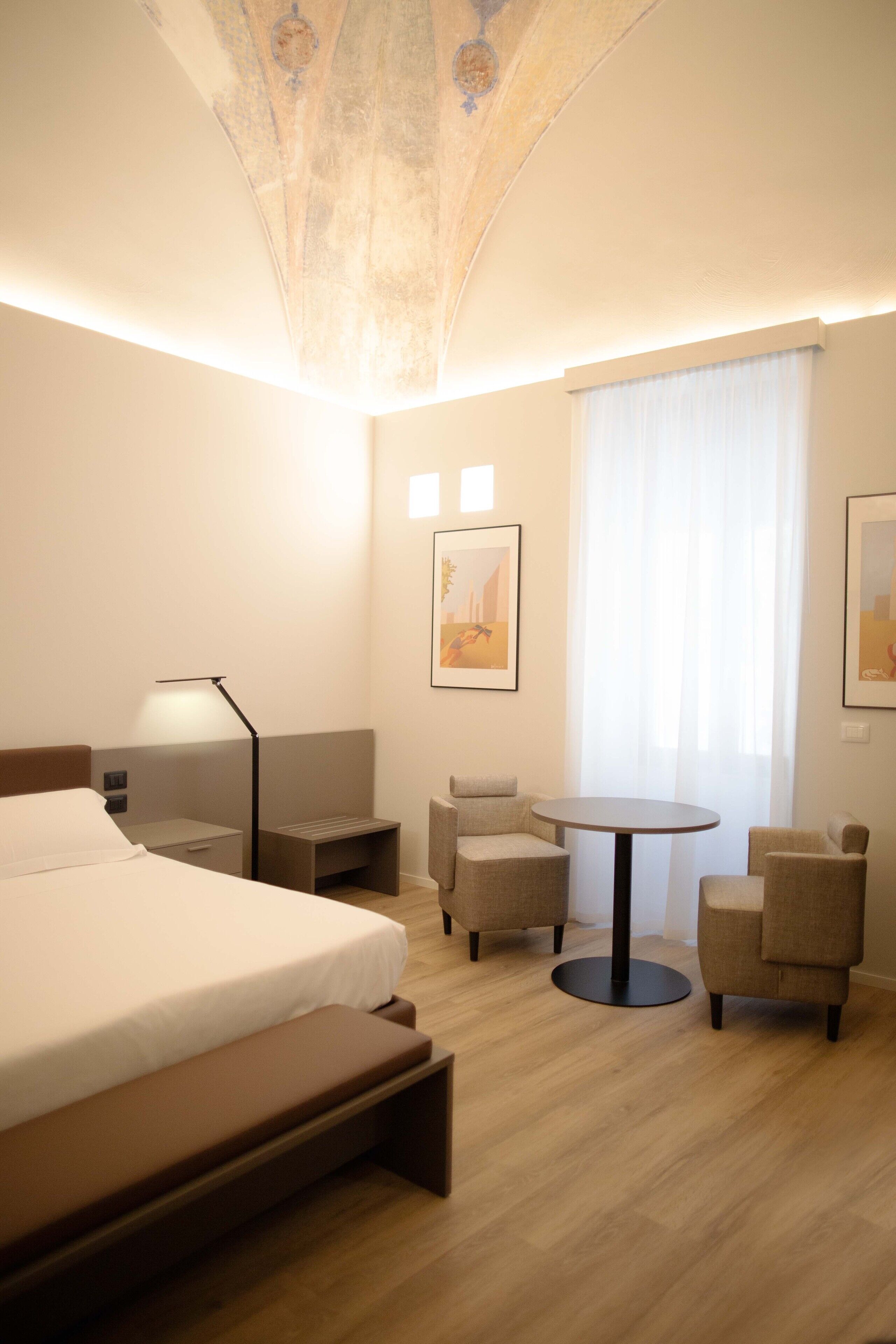 Une chambre d’hôtel avec un lit, un bureau, une chaise, une petite table et une fenêtre avec des rideaux.