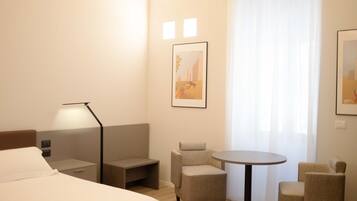 Une chambre d’hôtel avec un lit, un bureau, une chaise, une petite table et une fenêtre avec des rideaux.