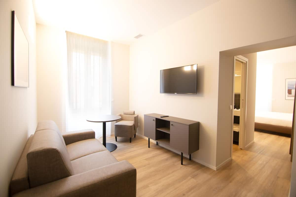 Un salon moderne avec un canapé, une petite table ronde, un meuble et un téléviseur fixé au mur.