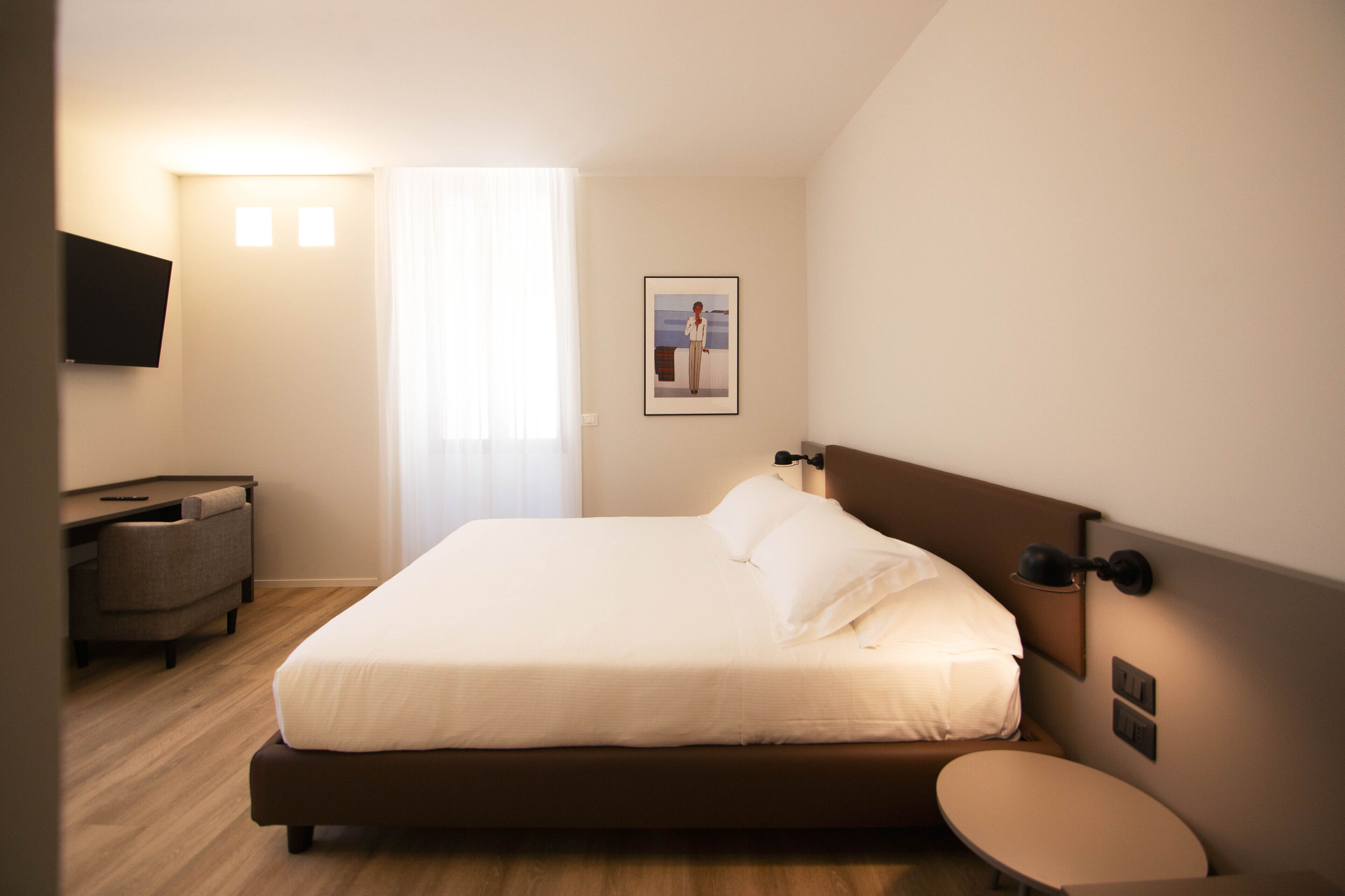 Een keurig opgemaakt slaapkamer met een bed, nachtkastje en een wandgemonteerde flatscreen-tv.