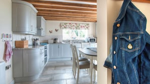 Une cuisine avec des meubles blancs, un plafond en bois et un coin repas comprenant une table et des chaises.