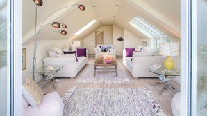 Un loft spacieux avec de hauts plafonds, des fenêtres de toit et un espace salon central agrémenté de canapés et d’une table basse.