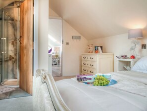 Een slaapkamer met een bed, een dressoir, een nachtkastje, een lamp en een deur die naar een andere kamer leidt.