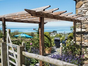 Een houten pergola met een stenen muur, met uitzicht op de kustlijn met huizen en een blauwe parasol.