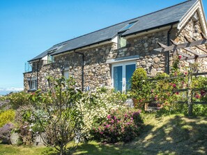 A stone house with a sloped roof, a wooden fence, and a garden with various plants and flowers. - 3 bedroom accommodation in Nefyn, Llyn Peninsula (Nefyn, Llyn Peninsula)
