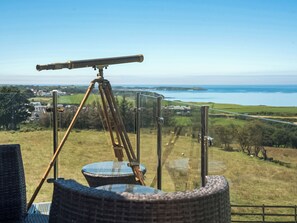 A telescope on a tripod, a wicker chair, and a view of a coastal landscape.