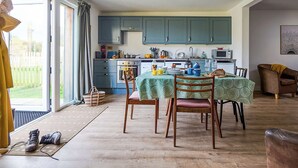 A modern kitchen with blue cabinets, a dining area with a table set for four, and a view of the outdoors through a sliding glass door. - 1 bedroom accommodation in Clynnog Fawr (Clynnog Fawr)