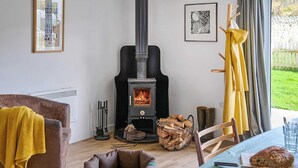 A cozy living room with a wood-burning stove, a comfortable armchair, a pet bed, and a dining table with bread. - 1 bedroom accommodation in Clynnog Fawr (Clynnog Fawr)