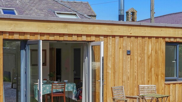 A wooden house with a sliding glass door leading to a dining area with a table and chairs. - 1 bedroom accommodation in Clynnog Fawr (Clynnog Fawr)