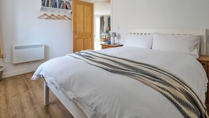 A bedroom with a large bed, a wooden door, a radiator, and a bookshelf with books and DVDs. - 1 bedroom accommodation in Clynnog Fawr (Clynnog Fawr)