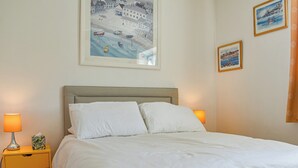 Cama bem arrumada com roupa de cama branca, cabeceira e duas mesas de cabeceira com abajures e uma caixa de lenços.