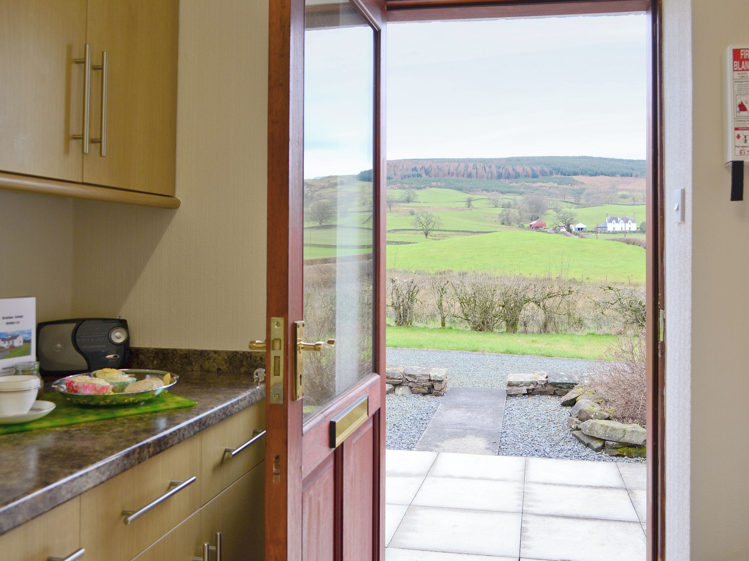 A kitchen with a view of a rural landscape through an open door.