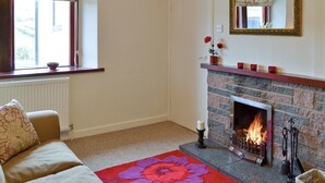 A cozy living room with a fireplace, a sofa, a window with floral curtains, and a mirror on the wall. - Beuchan Cottage Keir Mill (Keir Mill, Thornhill)