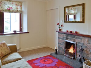 Una sala de estar acogedora con chimenea, un sofá, una ventana con cortinas florales y un espejo en la pared.