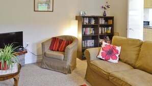 A living room with a sofa, a chair, a bookshelf, a television, and a small table with a plant. - Beuchan Cottage Keir Mill (Keir Mill, Thornhill)
