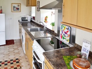 Una cocina con microondas, lavabo y horno. Hay un armario de madera sobre la encimera y un reloj en la pared.