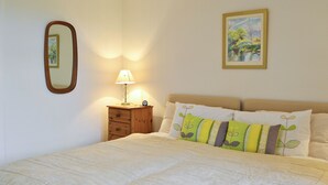 A neatly made bed with a quilted white duvet, a bedside lamp, a small wooden nightstand, and a framed painting on the wall. - Beuchan Cottage Keir Mill (Keir Mill, Thornhill)