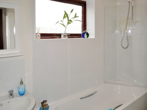 Een badkamer met een wit wastafelmeubel, een spiegel, een raam met een plant en een douchehoek.