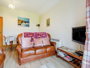 A living room with a brown leather sofa, a dining table with chairs, a TV, and a small table with books and a keyboard.