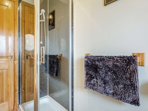 A bathroom with a glass shower enclosure, a wooden door, and a towel hanging on a towel rack.