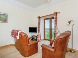 A room with two leather armchairs, a flat-screen TV, a small table with a remote control, and a floor lamp.