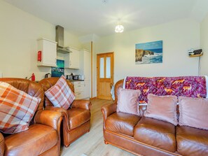 A living room with two brown leather sofas, a kitchen in the background, and a painting on the wall.
