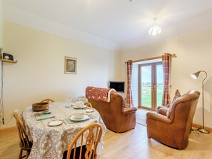 A dining area with a table set for four, two leather chairs, a television, and a view through a glass door.
