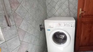 A white washing machine in a corner with a tiled wall and a wooden door. - Countryside italian villa, close to the sea (Jerzu)
