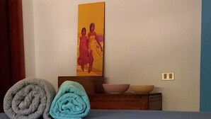 A bed with a blue quilt, two rolled towels in grey and teal, a wooden nightstand with a bowl, and a painting on the wall. - Countryside italian villa, close to the sea (Jerzu)